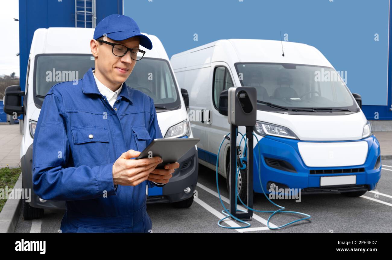 A man with a digital tablet stands next to electric delivery vans at electric vehicle charging station. High quality photo Stock Photo