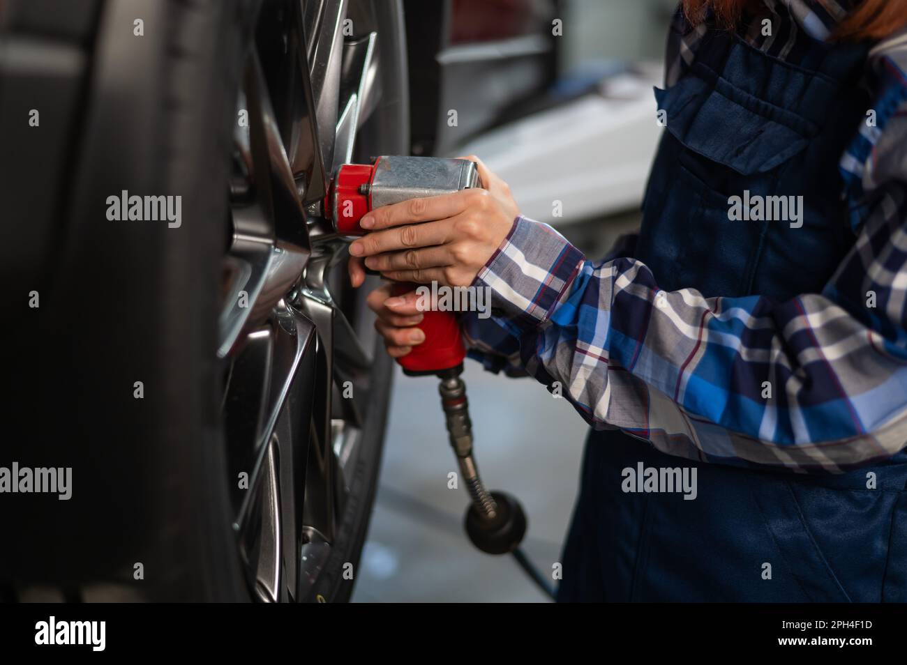 Woman mechanic uses pneumatic wrench to tighten the wheel nut. Girl at men's work Stock Photo