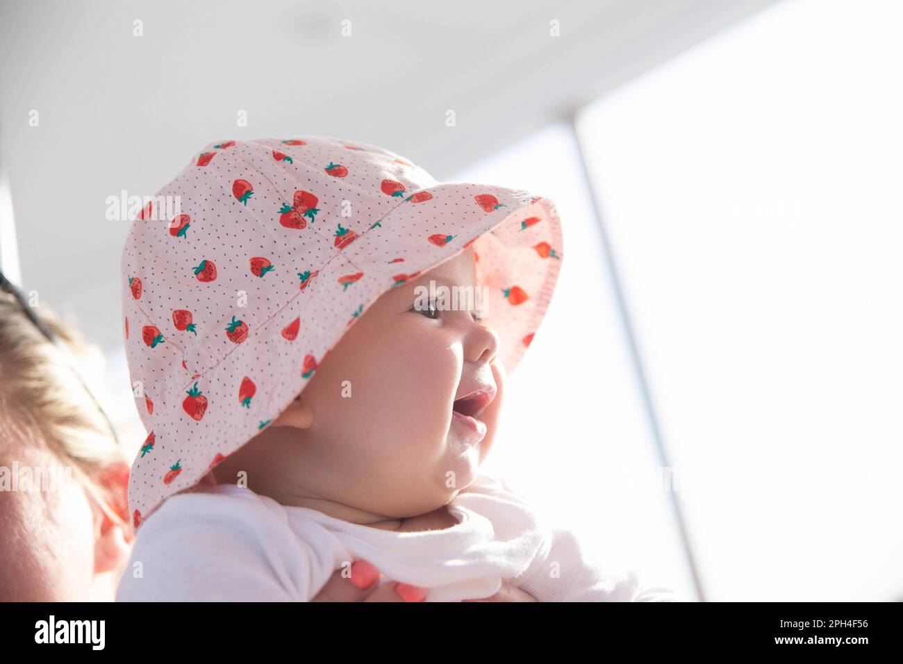 newborn girl in hat looks at the sunset and smiles toothlessly Stock Photo