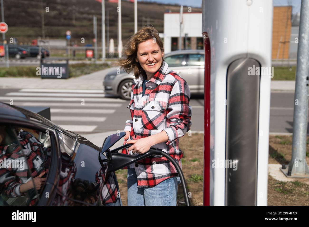 Woman in a plaid shirt charging an electric car. High quality photo Stock Photo