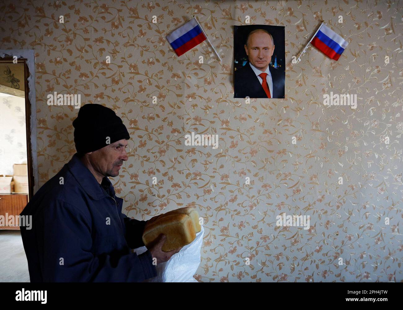 Local resident Nikolai carries bread delivered by volunteers, by a wall with a portrait of Russian President Vladimir Putin, in the course of Russia-Ukraine conflict in the settlement of Toshkivka, in the Luhansk region, Russian-controlled Ukraine, March 24, 2023. REUTERS/Alexander Ermochenko Stock Photo