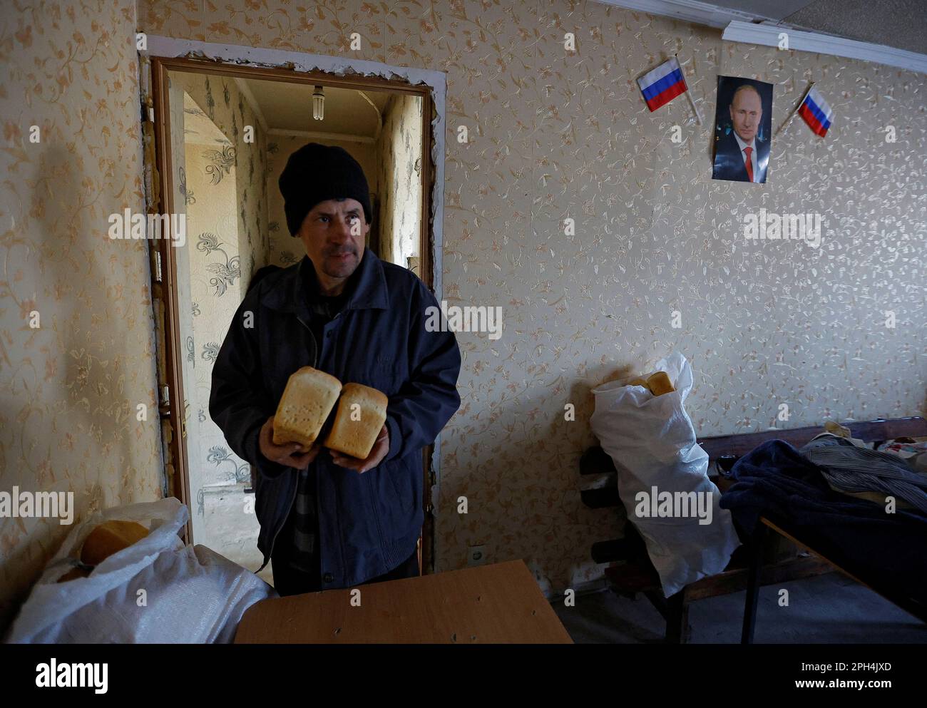 Local resident Nikolai holds bread delivered by volunteers, by a wall with a portrait of Russian President Vladimir Putin, in the course of Russia-Ukraine conflict in the settlement of Toshkivka, in the Luhansk region, Russian-controlled Ukraine, March 24, 2023. REUTERS/Alexander Ermochenko Stock Photo