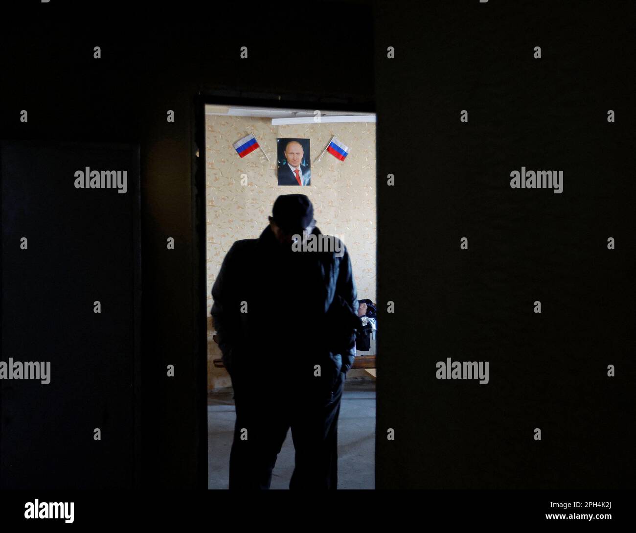 A man walks through a building where volunteers distribute aid to residents, as a portrait of Russian President Vladimir Putin hangs on a wall, in the course of Russia-Ukraine conflict in the settlement of Toshkivka, in the Luhansk region, Russian-controlled Ukraine, March 24, 2023. REUTERS/Alexander Ermochenko Stock Photo