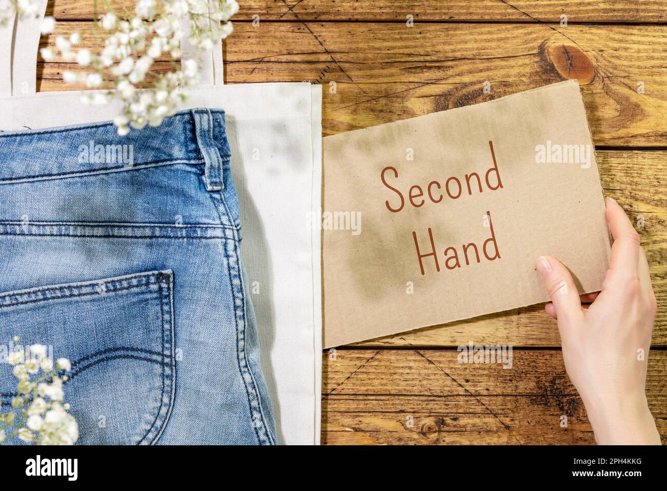 Sustainable still life with jeans on textile bag and female hand holding inscription second hand. Second hand shop. Circular fashion, eco friendly sus Stock Photo