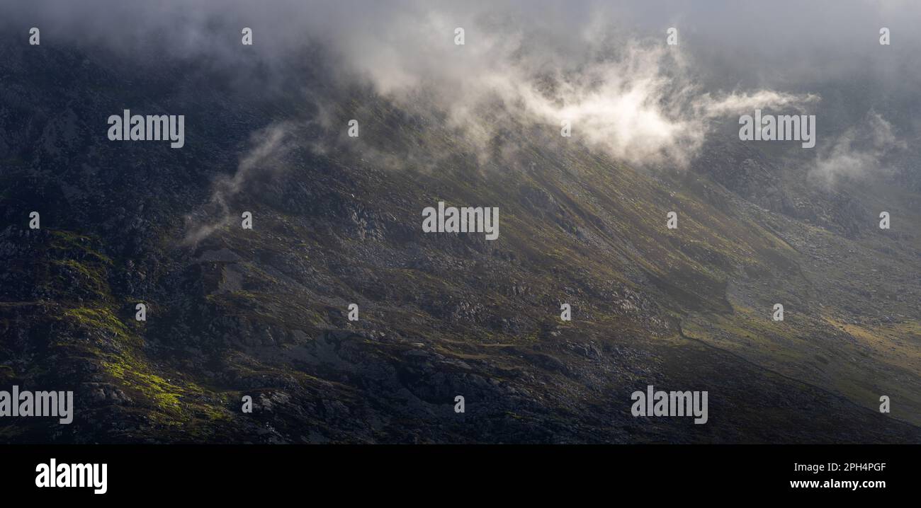 A mountainside with a patch of sunlight and low hanging clouds Stock ...