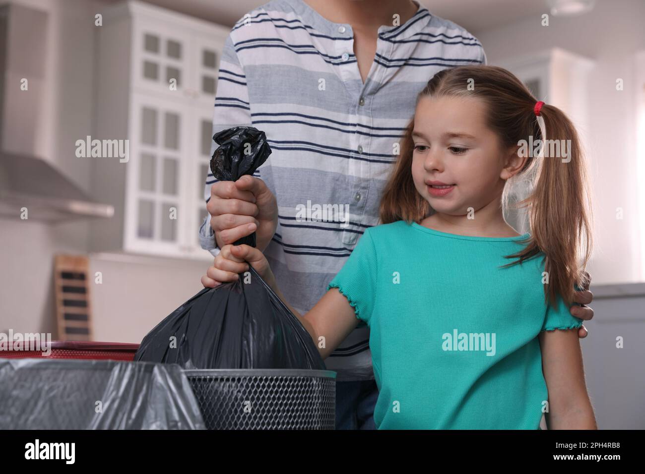 Little girl taking garbage bag out of bin in kitchen. Separate waste