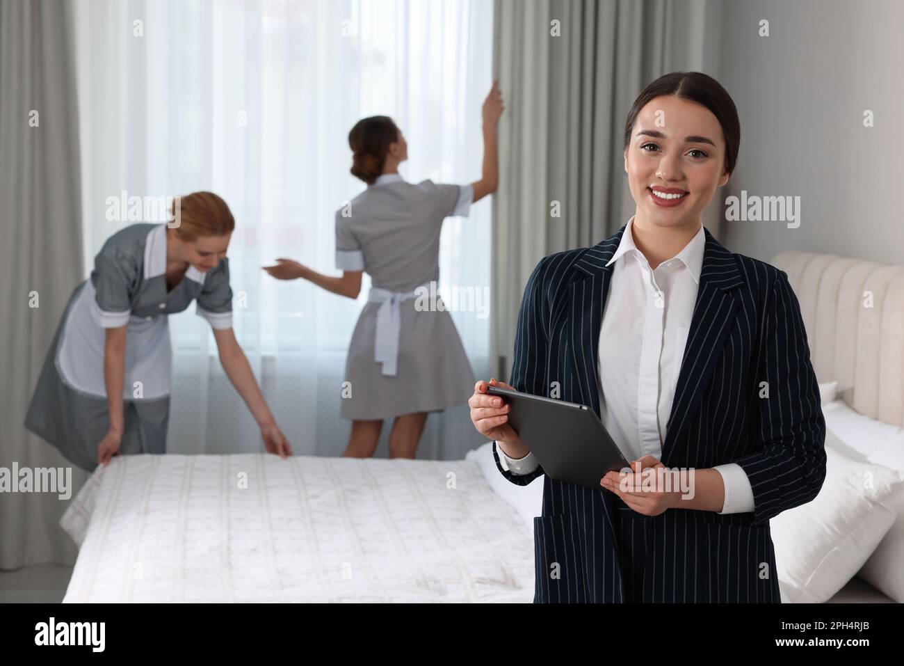Housekeeping manager with tablet checking maid's work in hotel bedroom