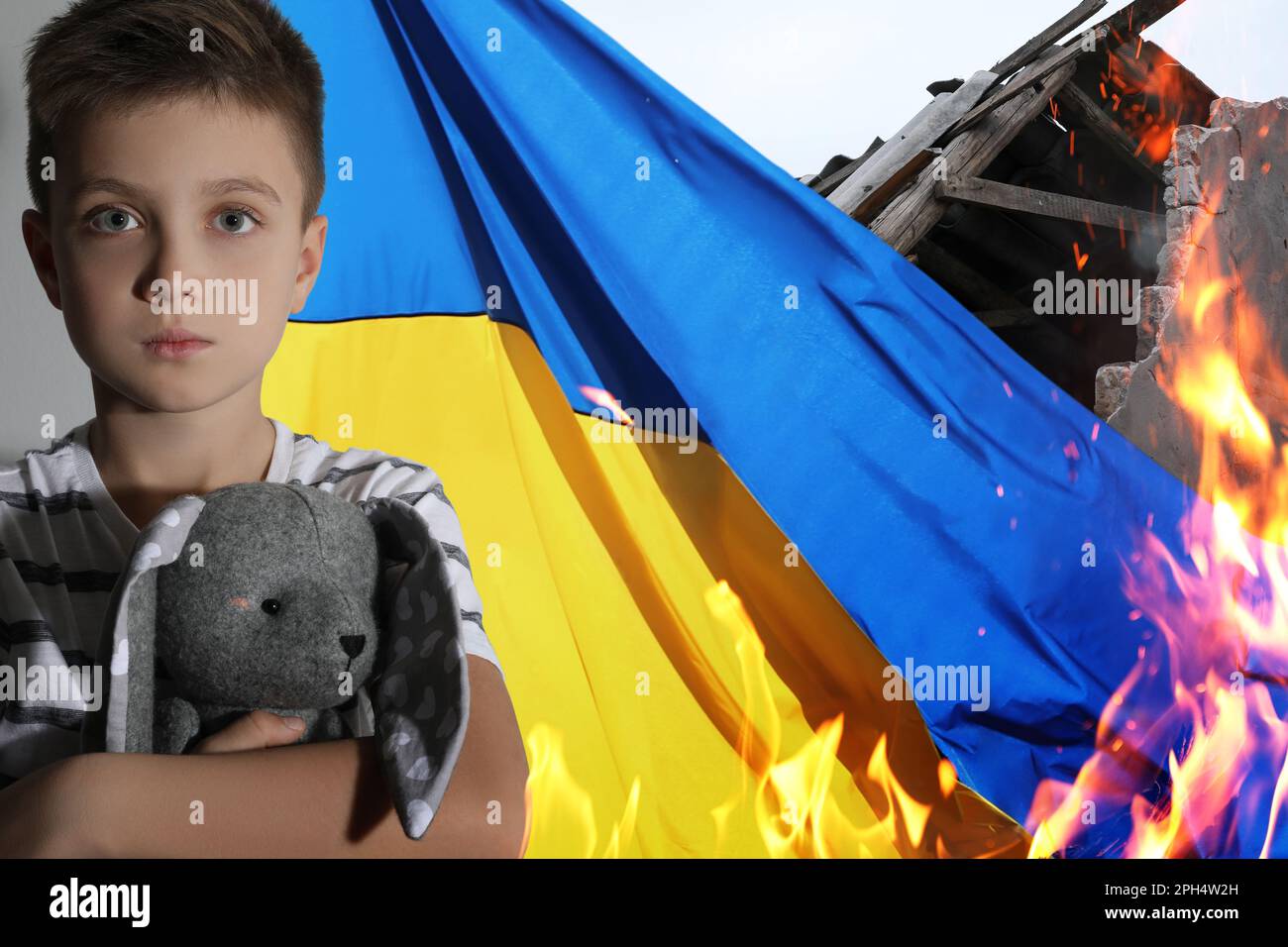 Sad little boy with toy, national flag and ruined house on fire. Stop war in Ukraine Stock Photo