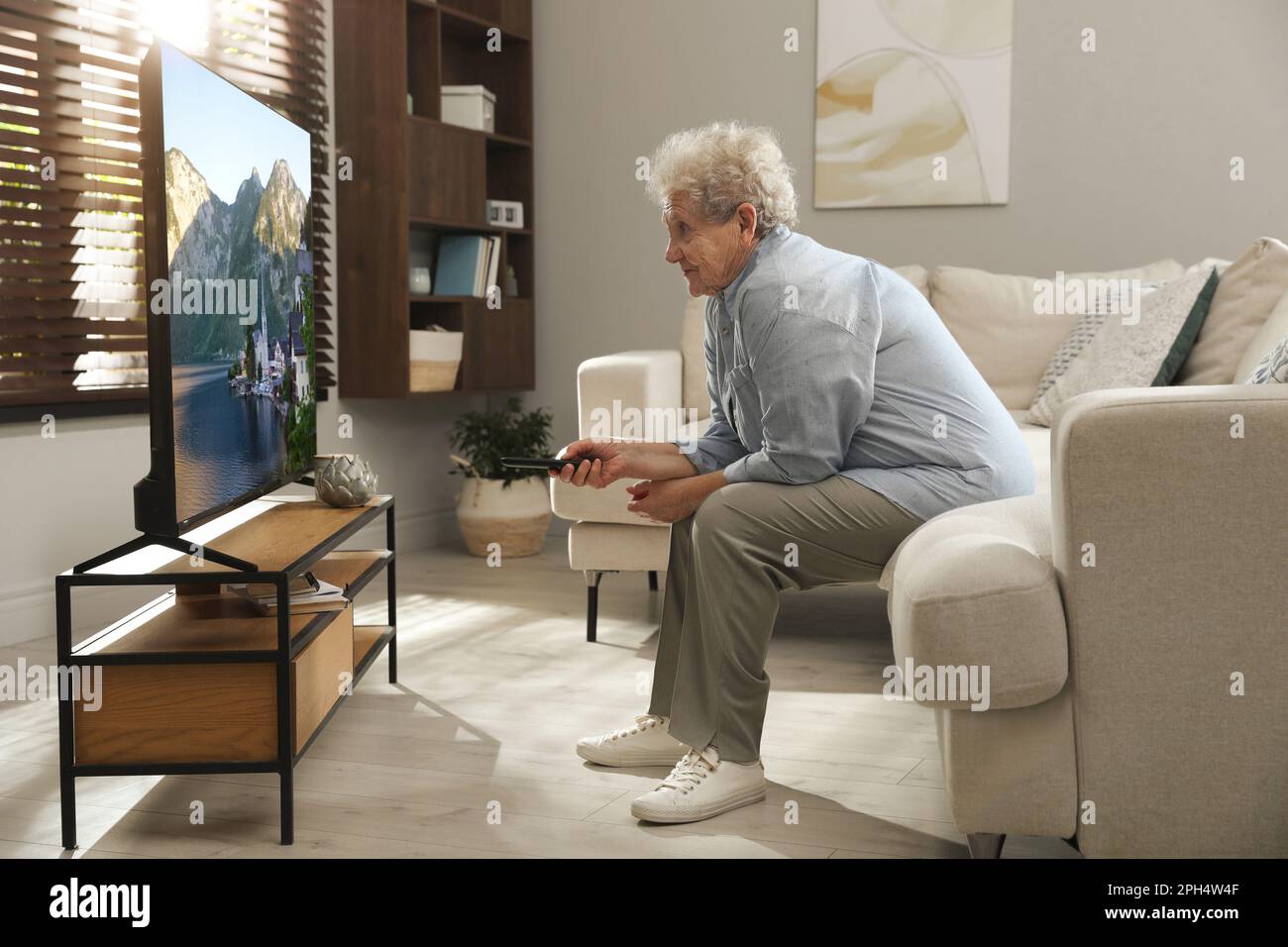 Elderly woman with poor posture watching TV in living room Stock Photo