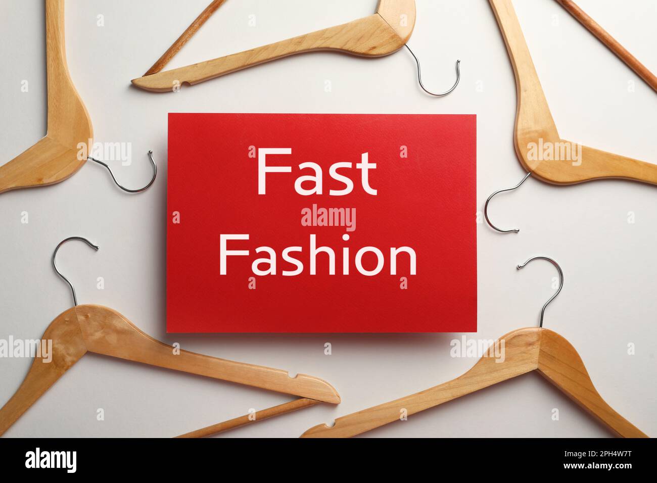 Red card with phrase Fast Fashion and wooden hangers on white background, top view Stock Photo