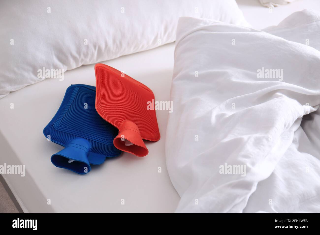 Different hot water bottles on white bed Stock Photo Alamy