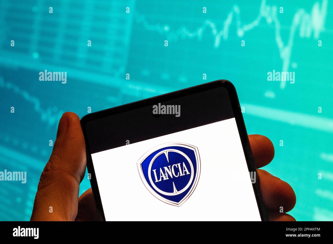 China. 15th Feb, 2023. In this photo illustration, the Italian automobile manufacturer Lancia logo seen displayed on a smartphone with an economic stock exchange index graph in the background. (Credit Image: © Budrul Chukrut/SOPA Images via ZUMA Press Wire) EDITORIAL USAGE ONLY! Not for Commercial USAGE! Stock Photo