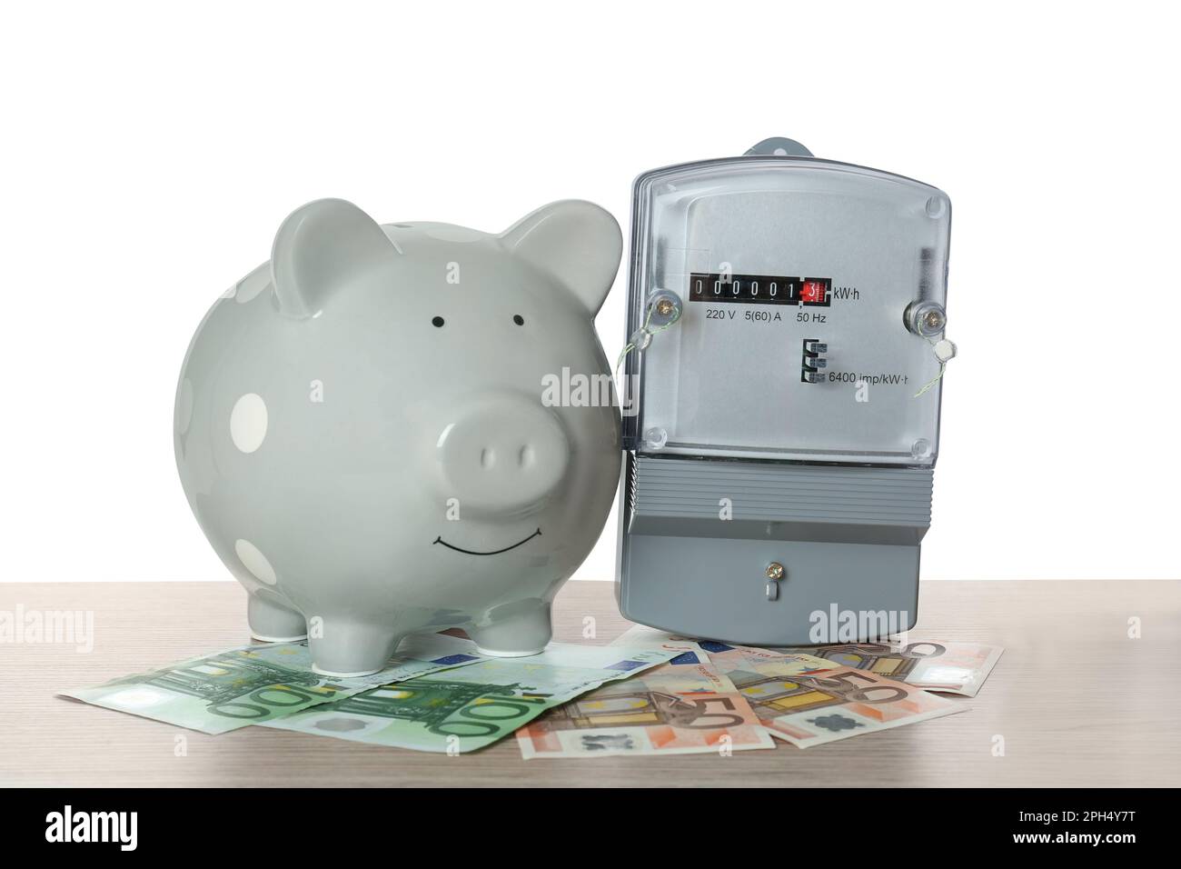 Electricity meter, piggy bank and money on wooden table against white ...