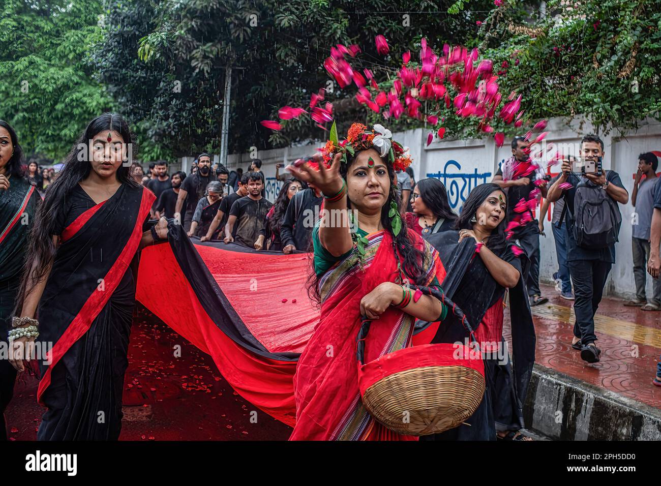 An artist seen throwing flowers during a performance of Lal Jatra (Red Procession) as it stages at the Dhaka University campus. Prachyanat School of Acting and Design held a procession of Lal Jatra (Red Procession), to remember the genocide by Pakistani Army on March 25, 1971 in Dhaka, Bangladesh on March 25, 2023. On this black night in the national history, the Pakistani military rulers launched ''Operation Searchlight'' killing some thousand people in that night crackdown alone. As part of the operation, tanks rolled out of Dhaka cantonment and a sleeping city woke up to the rattles of gun Stock Photo