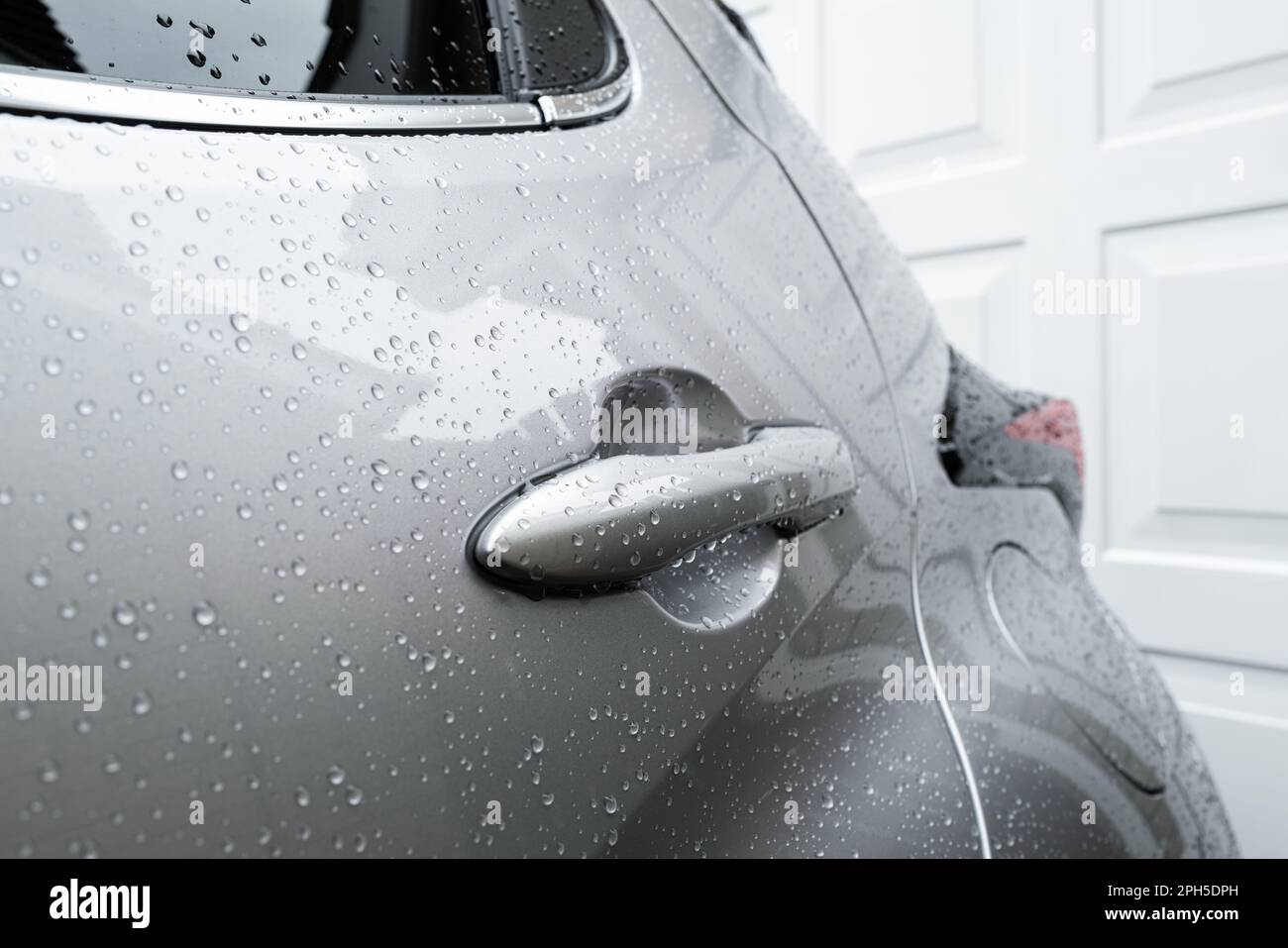 Shallow focus of the rear car door handle of a hybrid city car. Seen after a car wash the car is positioned in front of a garage door. Stock Photo