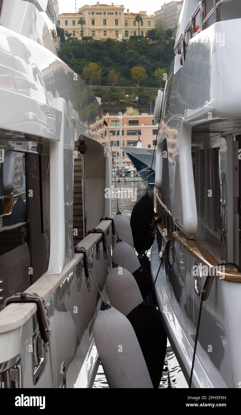 Monaco hillside seen between two super yachts moored at Monte Carlo in  the Port Hercule. Stock Photo