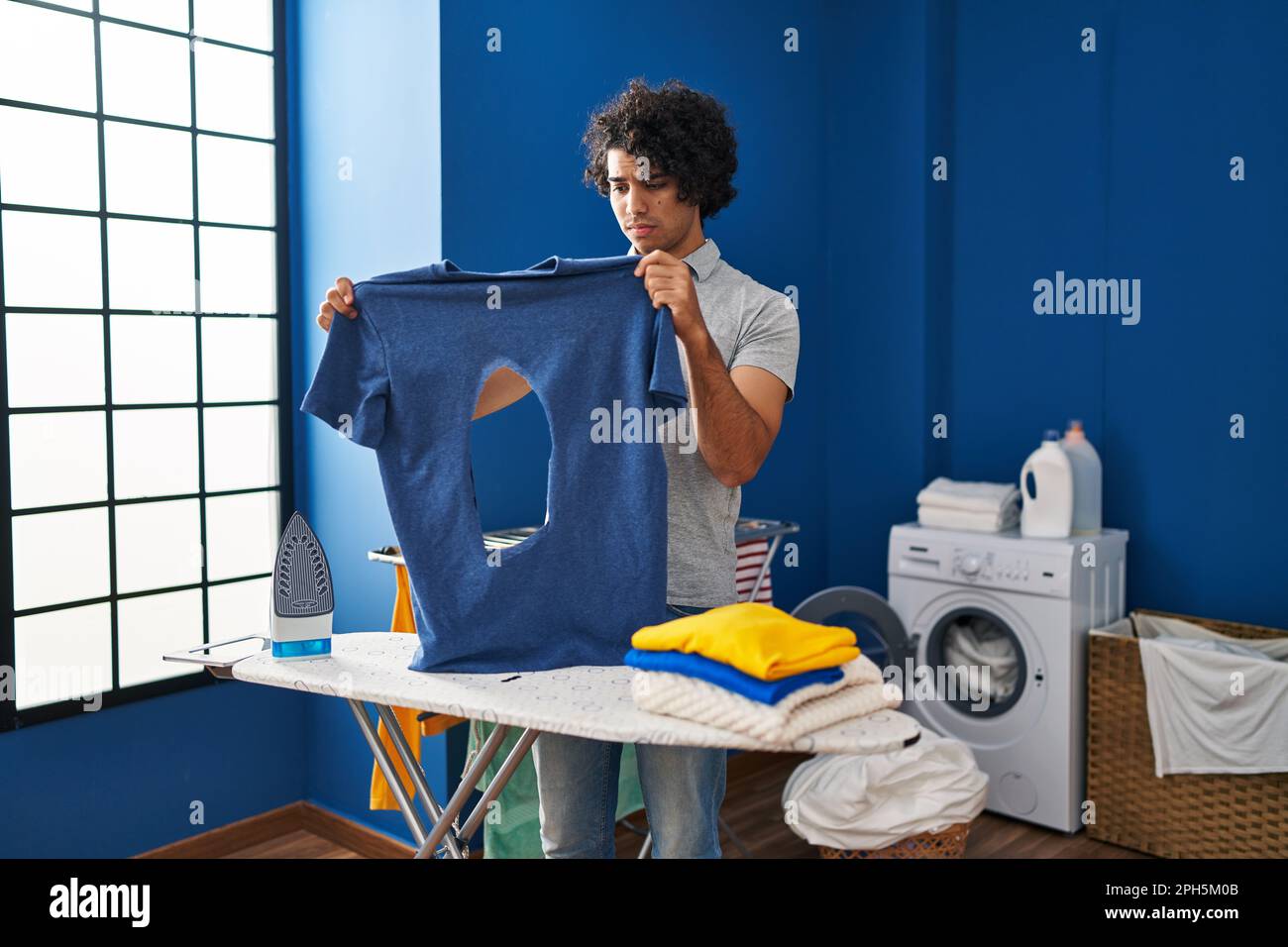 Hispanic man with curly hair ironing holding burned iron shirt at