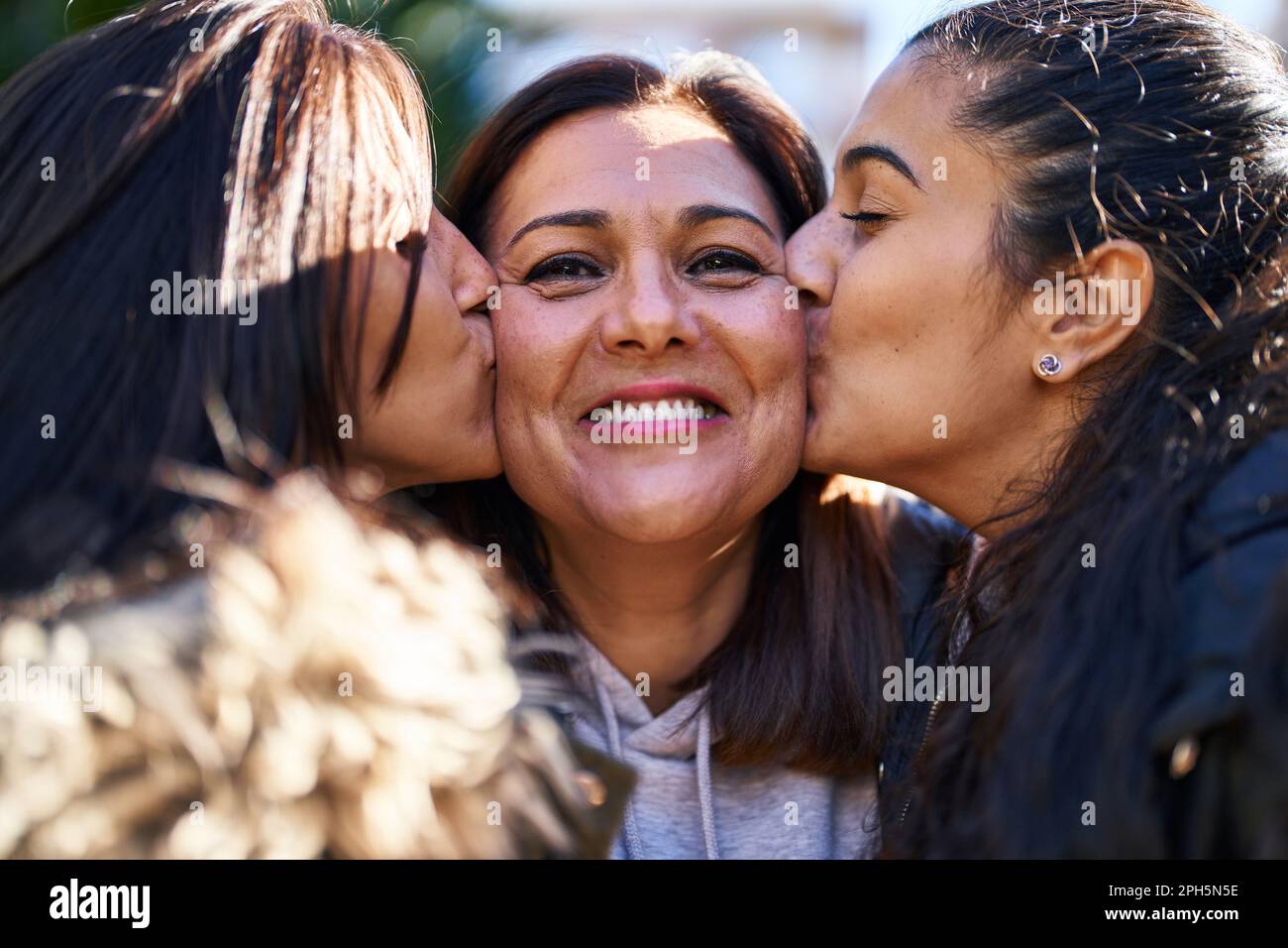 Three woman mother and daughters standing together and kissing at park