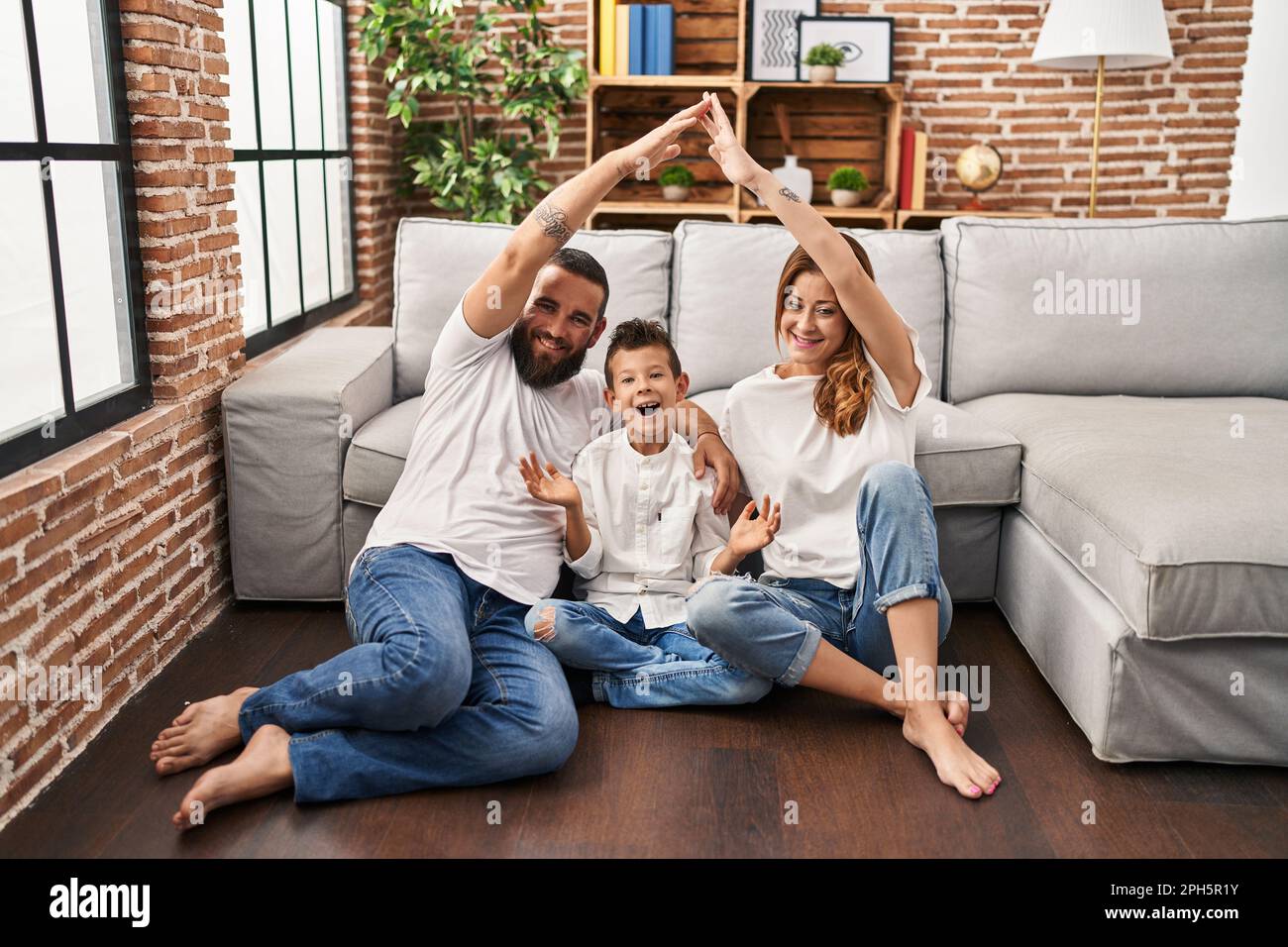 Family of three doing house shape with arms celebrating achievement with happy smile and winner expression with raised hand Stock Photo