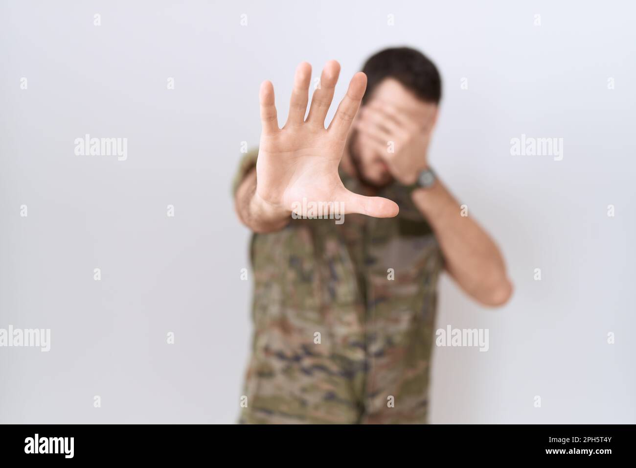 Young hispanic man wearing camouflage army uniform covering eyes with hands and doing stop gesture with sad and fear expression. embarrassed and negat Stock Photo