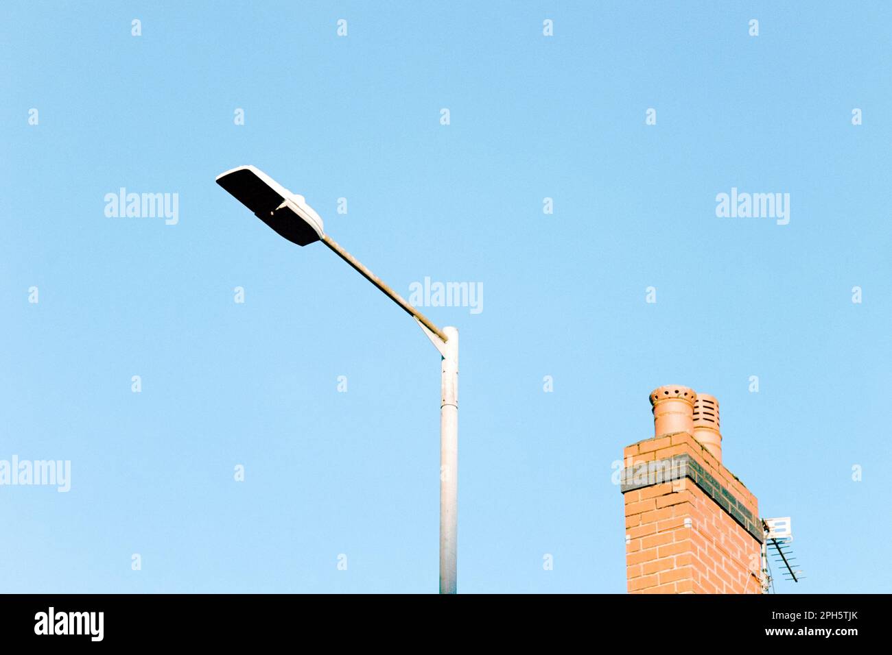 Minimalist photo of a street lamp and chimney from a nearby roof against a blue sky, England, UK, with copy space Stock Photo