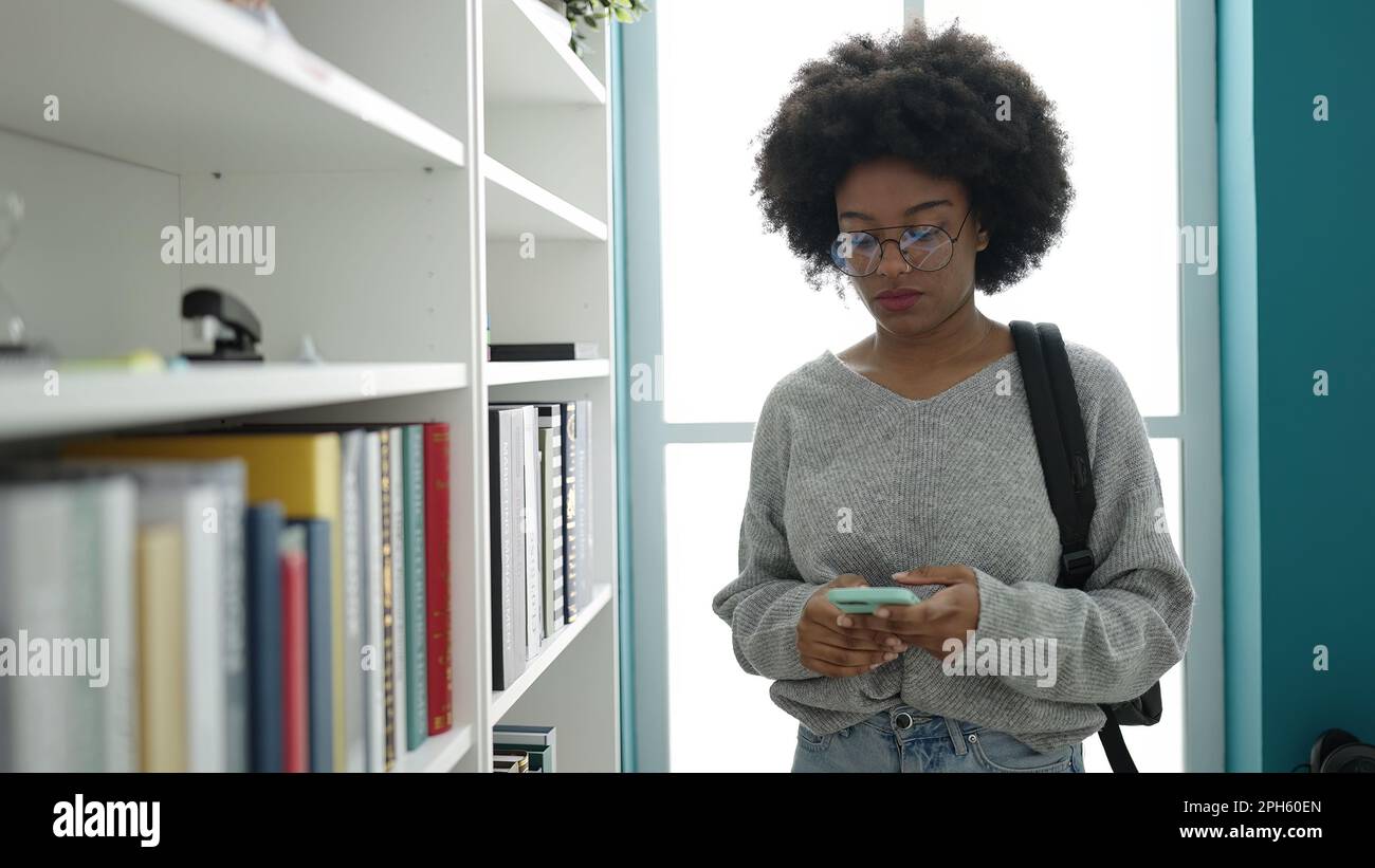 African american woman student using smartphone at library university ...