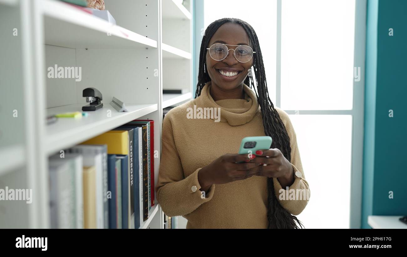 African woman smiling using smartphone at library university Stock ...