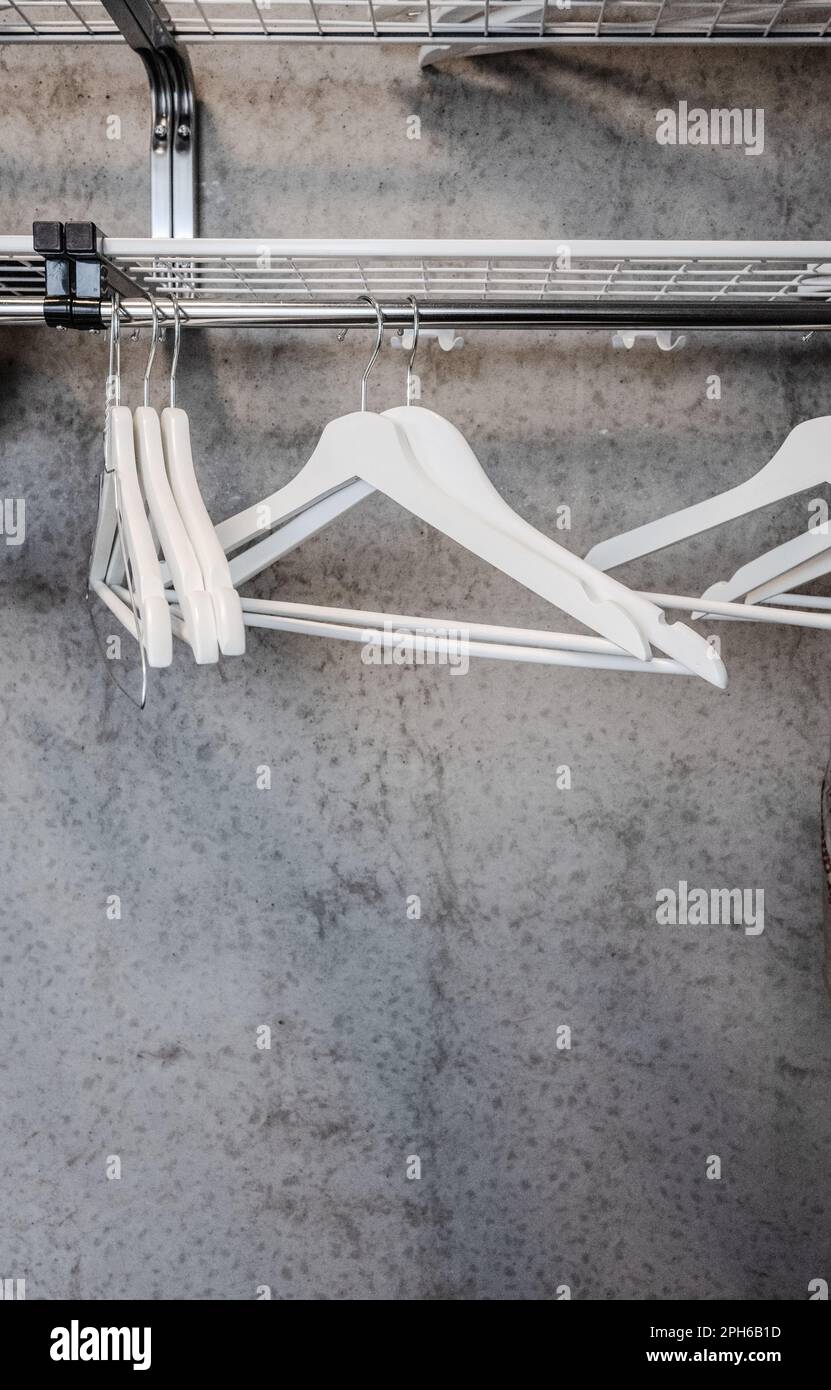 White clothes hangers on a rack with concrete wall behind Stock Photo