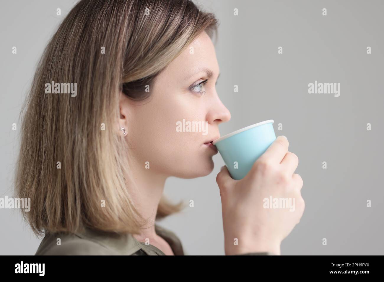 Blonde woman drinks coffee from blue paper cup in morning Stock Photo