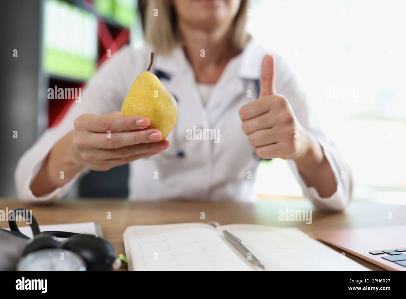 Doctor holds ripe pear in hand making thumb up gesture Stock Photo