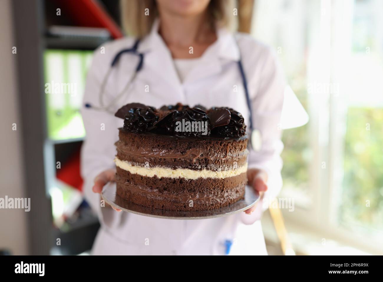 Doctor holding unhealthy delicious chocolate cake in clinic Stock Photo