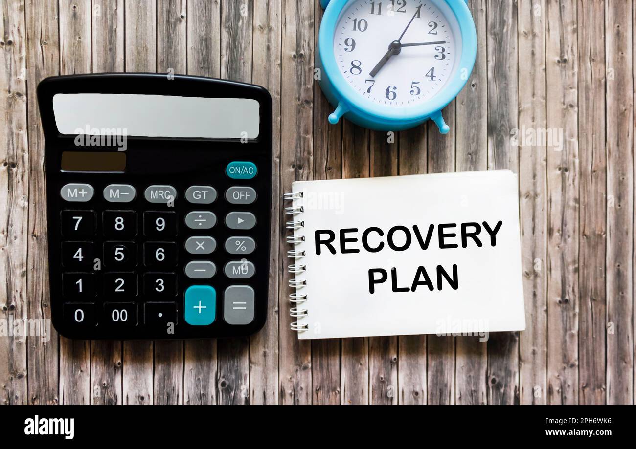 RECOVERY PLAN text in notepad on wooden table near calculator and clock, business concept Stock Photo