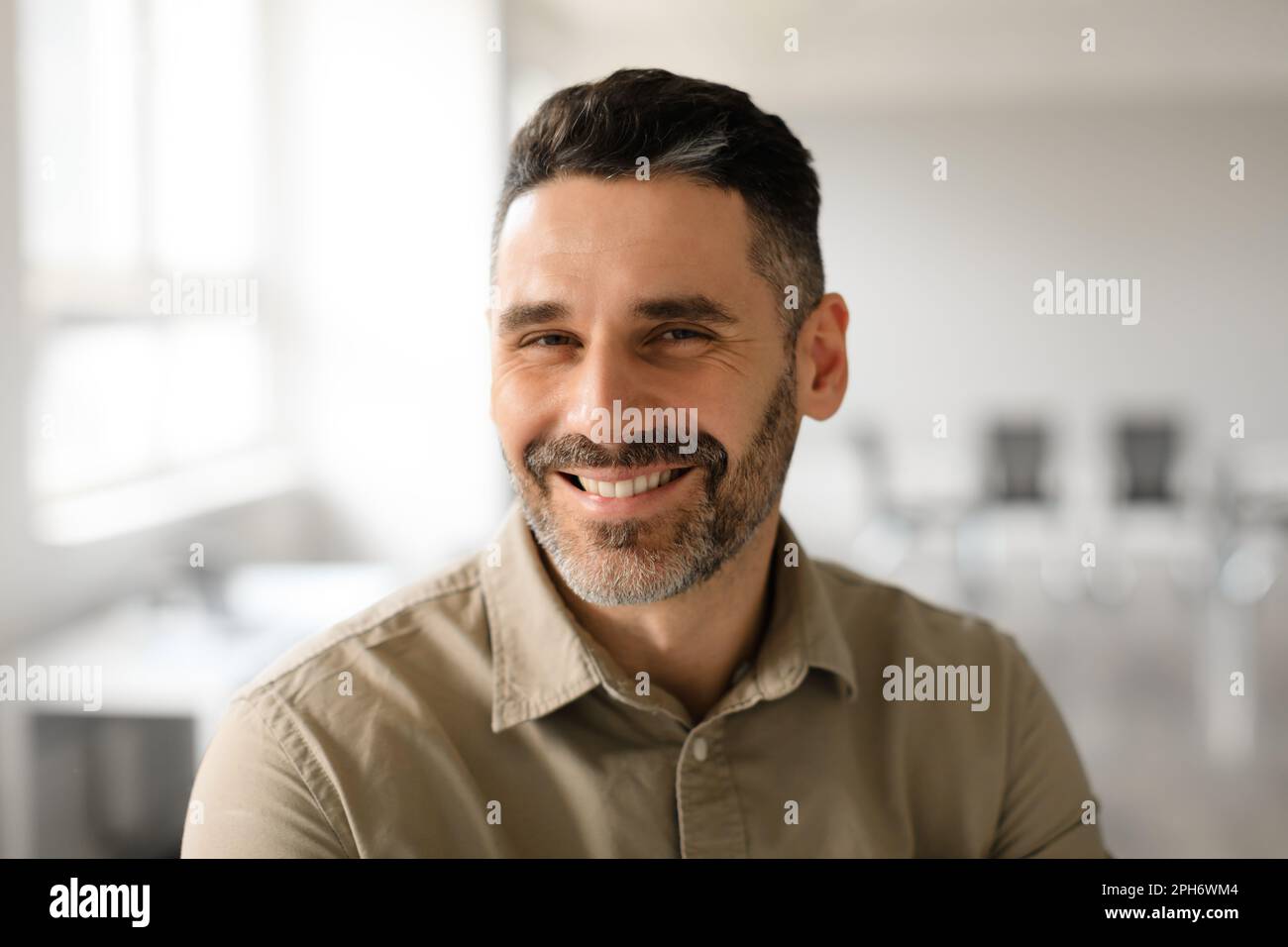 Portrait of well dressed middle aged businessman smiling confidently while standing in light modern office interior Stock Photo