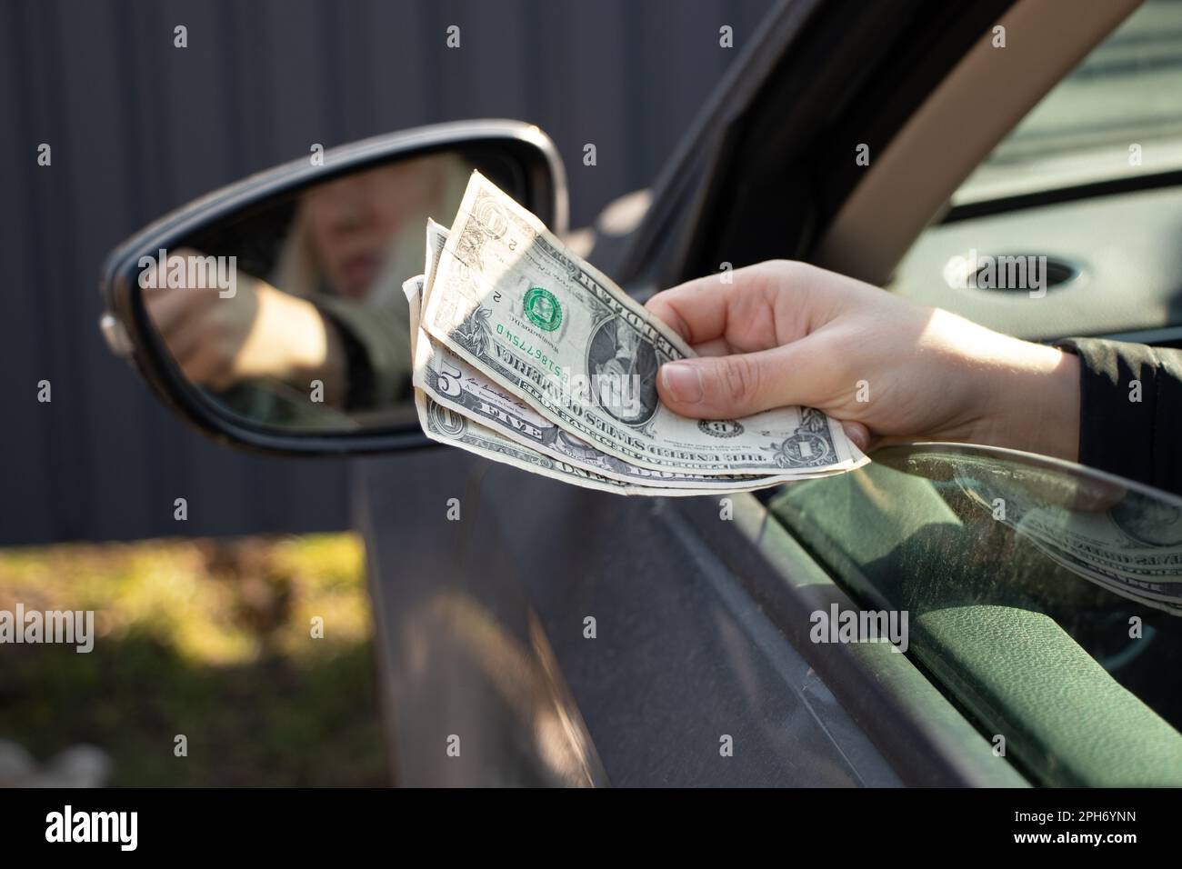 a woman's hand pulls out a dellara from a car window, corruption and bribes on the road Stock Photo