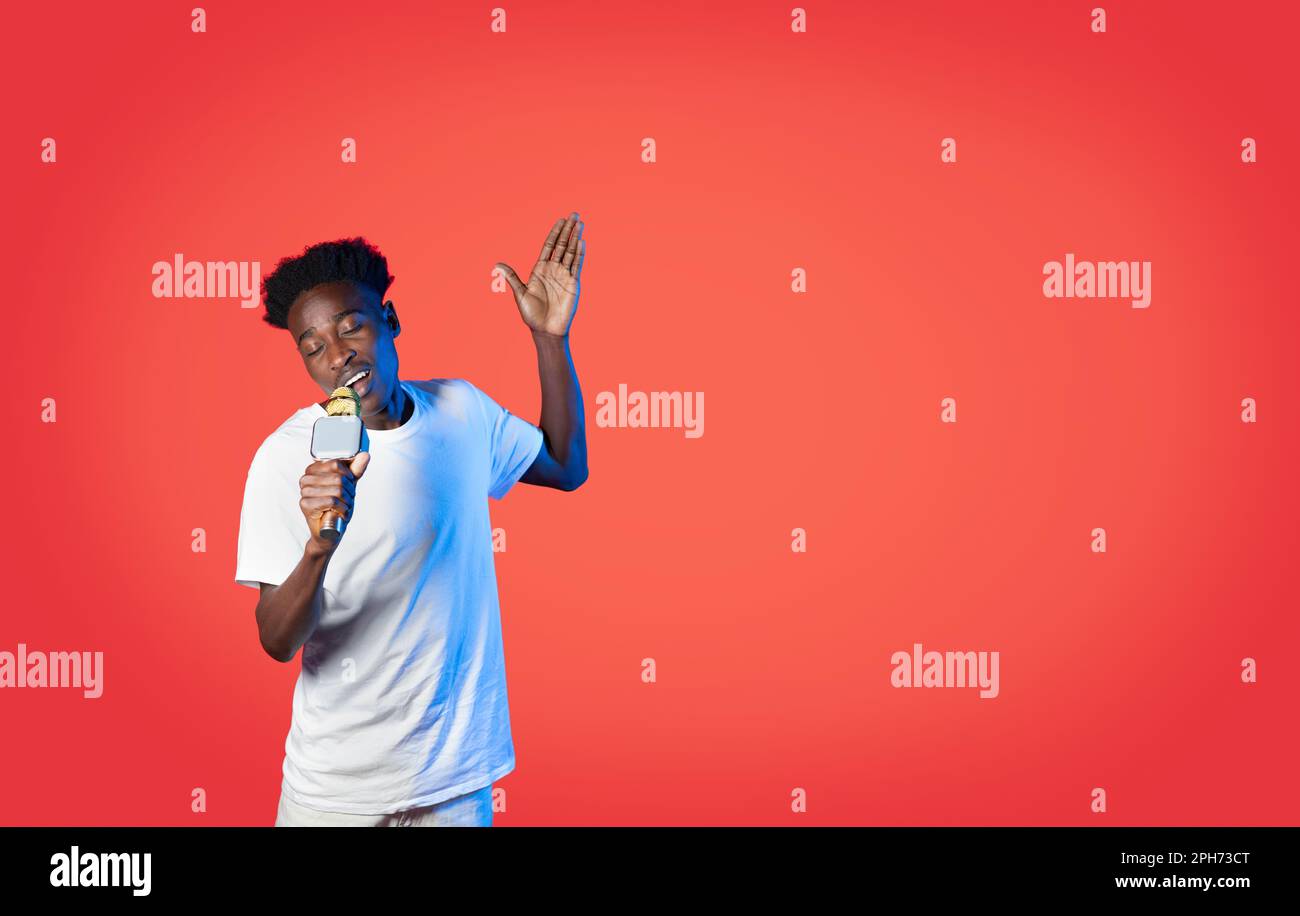 Handsome black guy singing with closed eyes, using microphone Stock