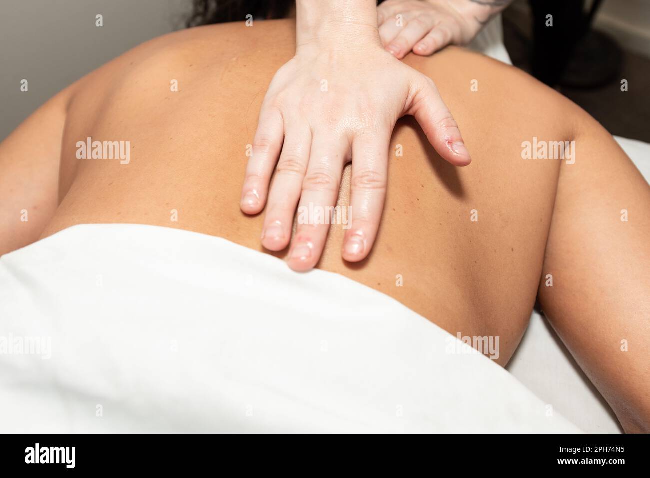 Massage therapist strong hands provide long and steady palm pressure on muscle stimulating strokes. Stock Photo