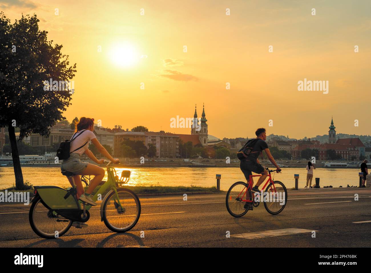 Bicyclists riding along river against sunset in old city Stock Photo