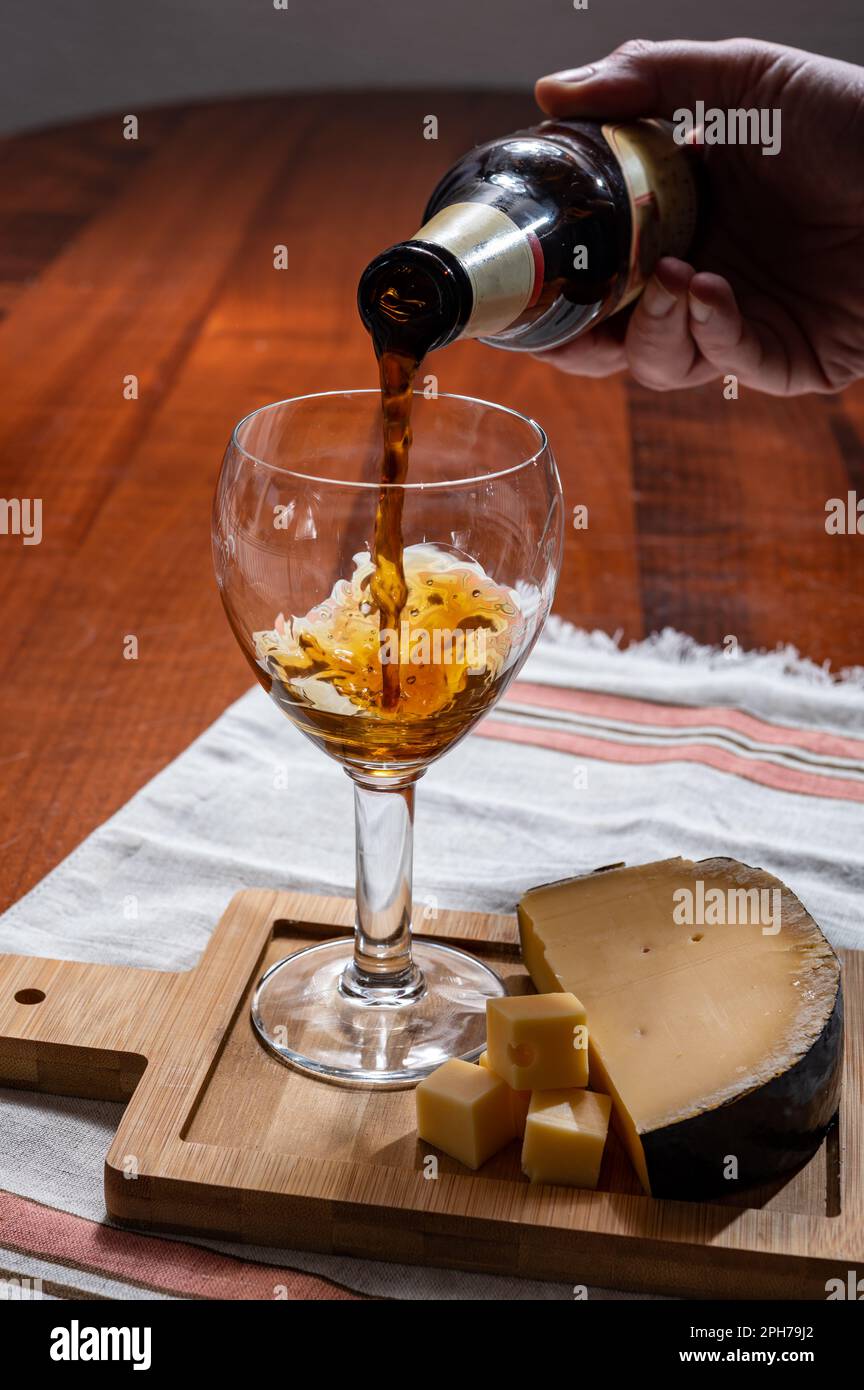 Pouring of Belgian abbey brown beer in glass and wooden board with old