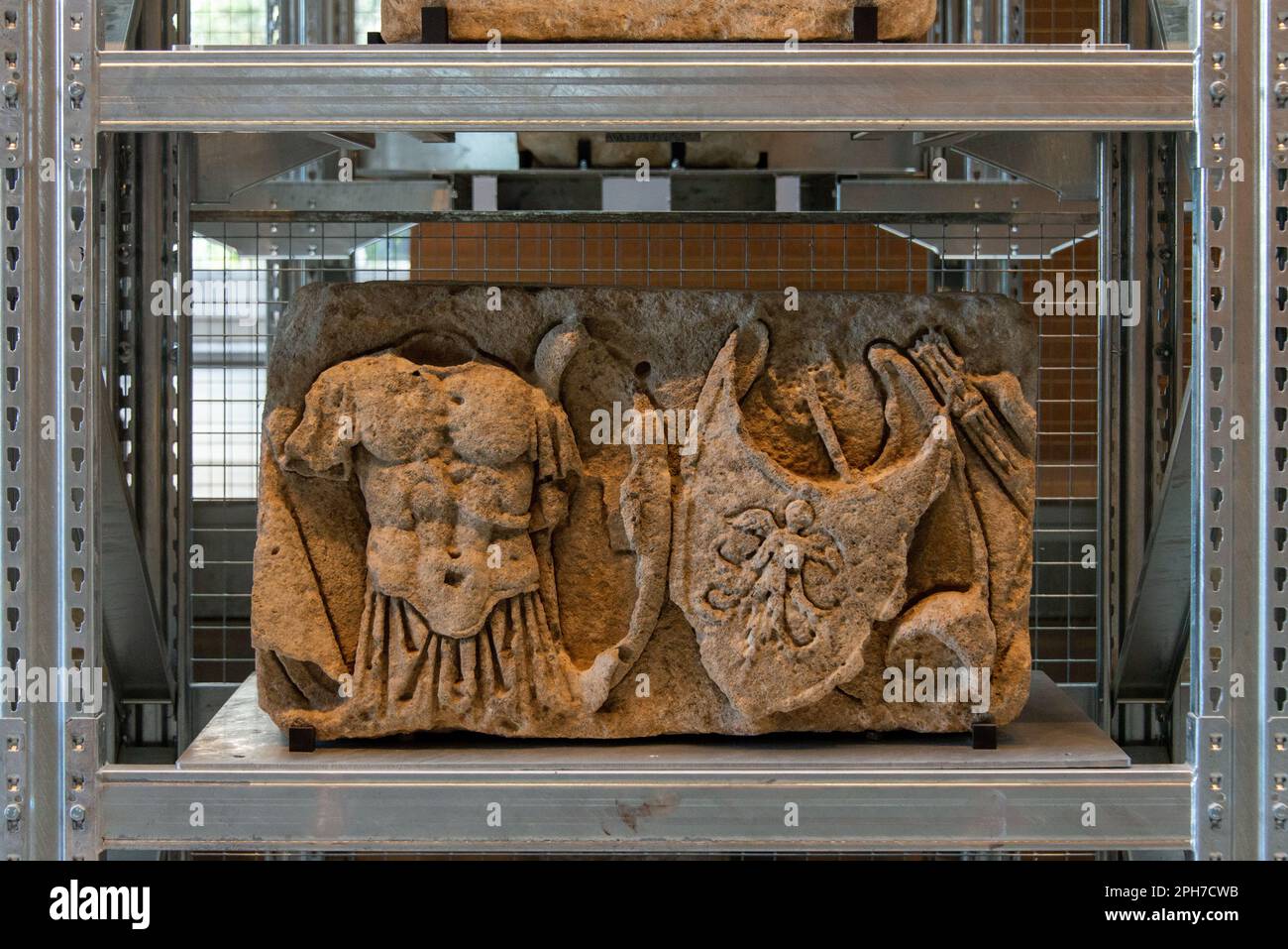 A carved relief stone with armour from a Roman tomb on the shelf of the impressive Lapidary Wall at Narbo Via Roman History Museum in Narbonne. Stock Photo