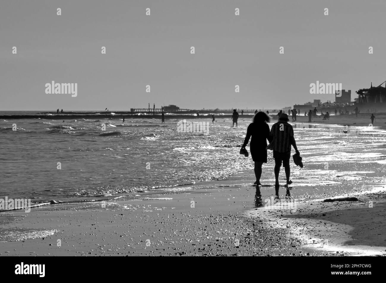 Galveston, Texas, USA - February 2023: Silhouette of two perople strolling barefoot along the water's edge in evening sun Stock Photo