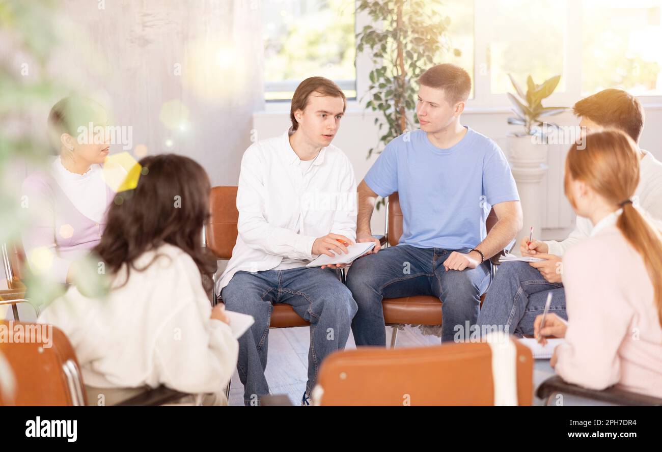Cheerful young student discussing learning assignment with coursemates Stock Photo