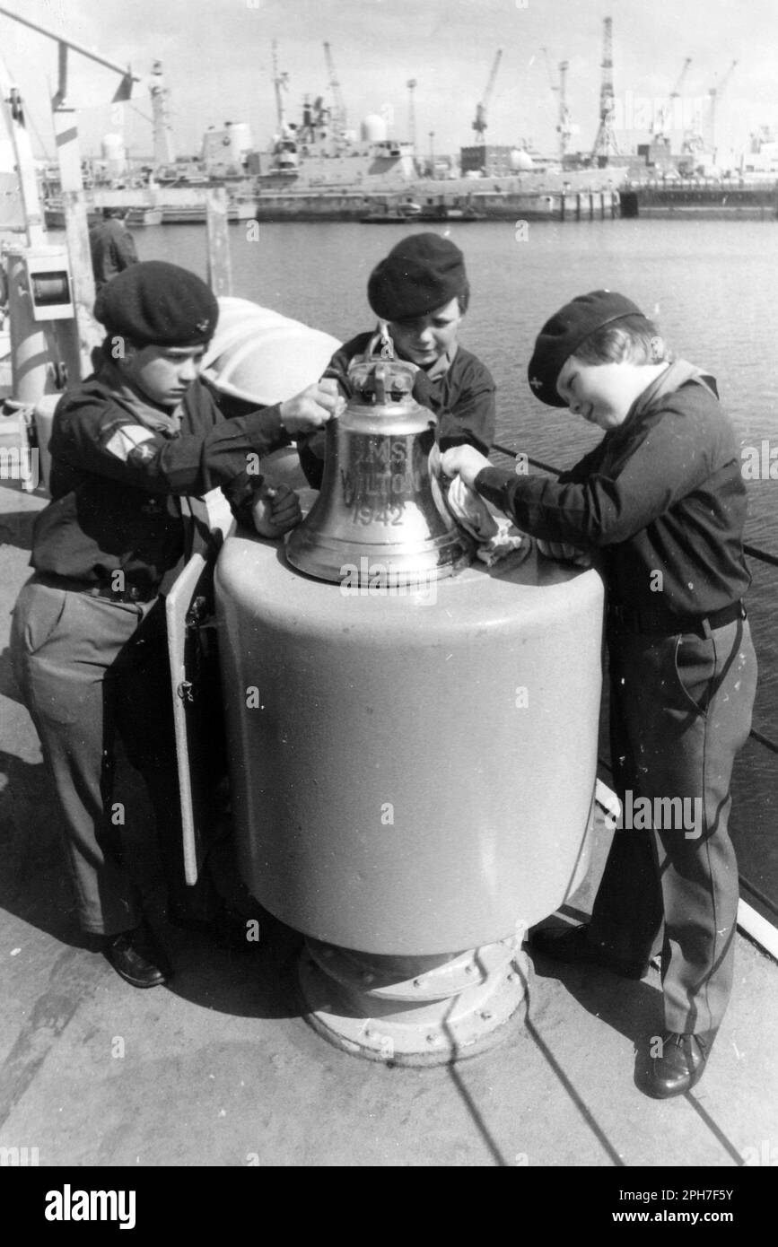 BOY SCOUTS FROM THE ISLE OF WIGHT POLISH THE BELL OF HMS WILTON IN PORTSMOUTH NAVY BASE AT THE START OF THEIR BOB A JOB WEEK. L TO R. GARY POORE, ROSS FORBES AND BARRY ROBINSON. PIC MIKE WALKER 1985 Stock Photo