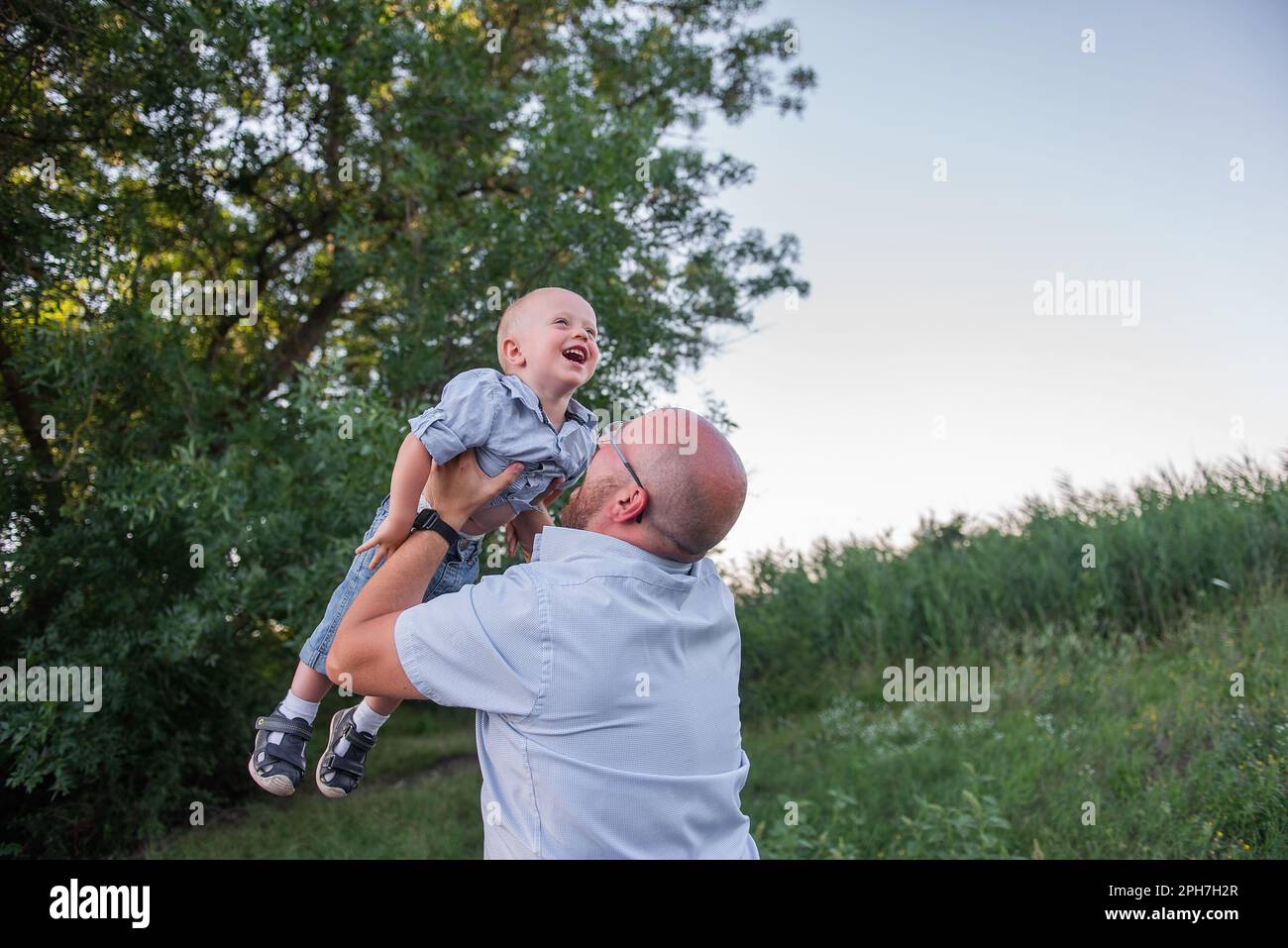 Bald man with glasses throws child into the sky air. Father in jeans