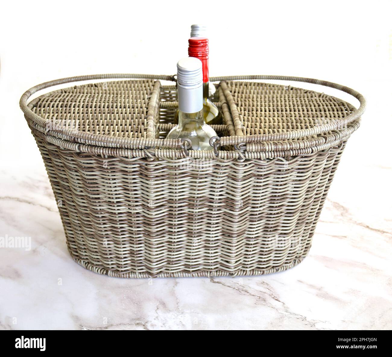 Wicker picnic basket with wine compartments, wine bottles on marble and