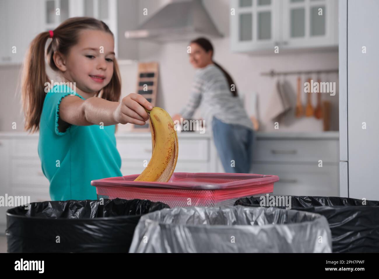 Little girl throwing banana peel into trash bin in kitchen. Separate waste collection Stock Photo