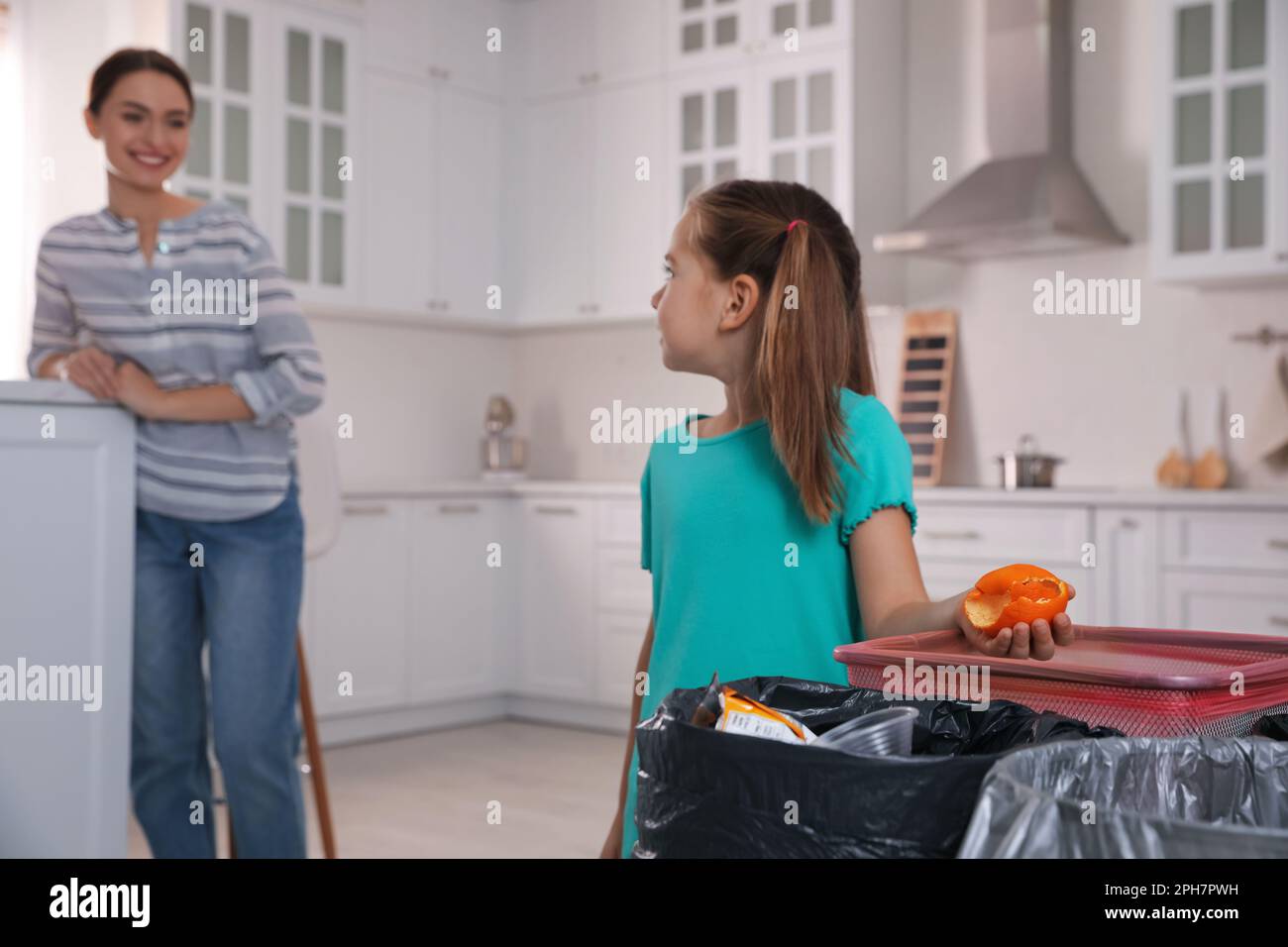Little girl throwing tangerine peel into trash bin in kitchen. Separate waste collection Stock Photo