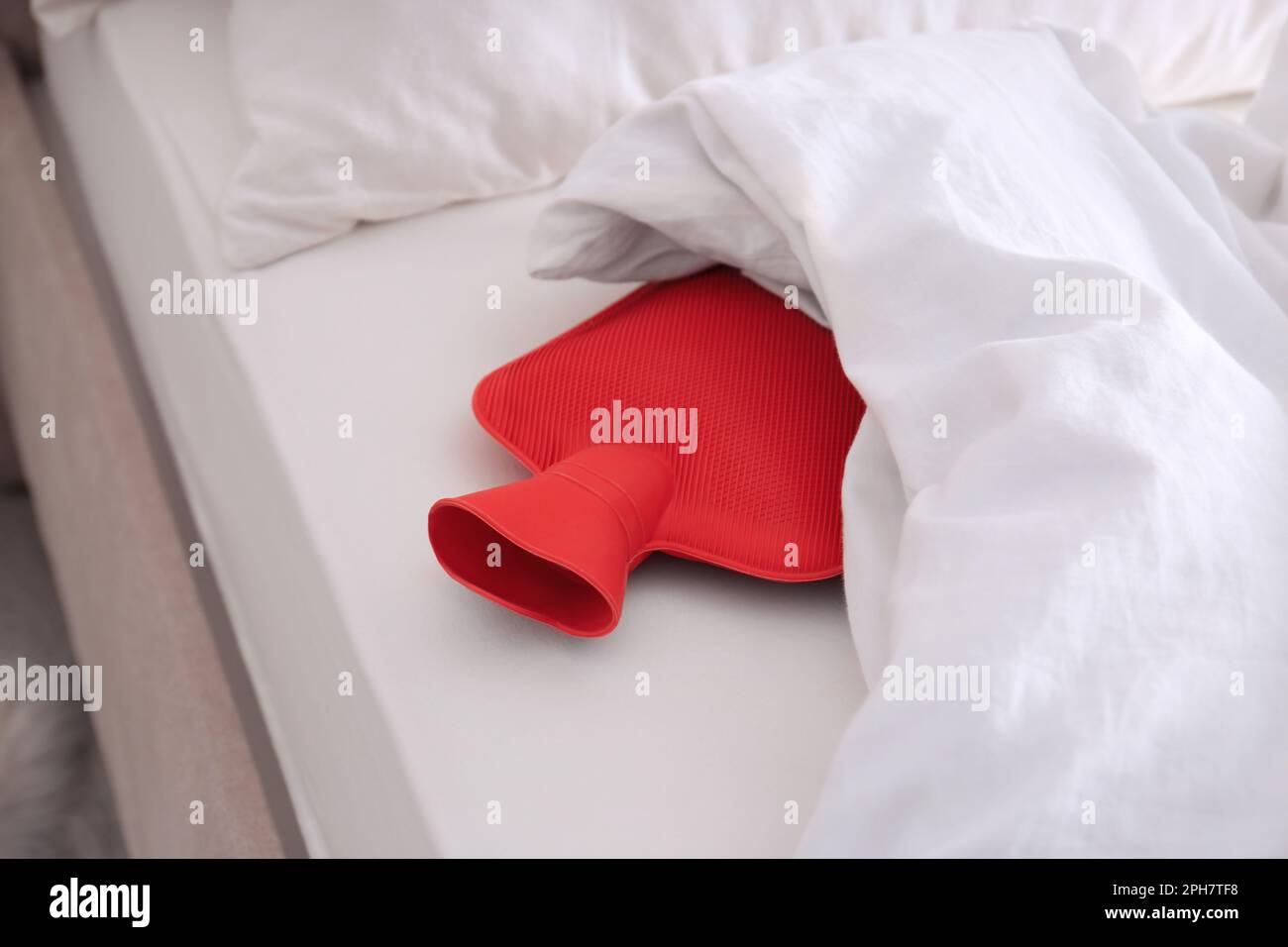 Red hot water bottle in bed indoors Stock Photo Alamy