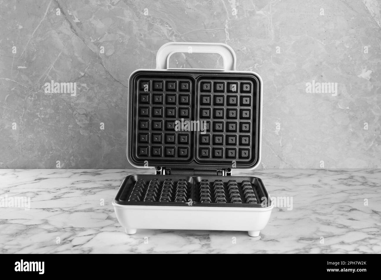 Open electric waffle maker on white marble table Stock Photo