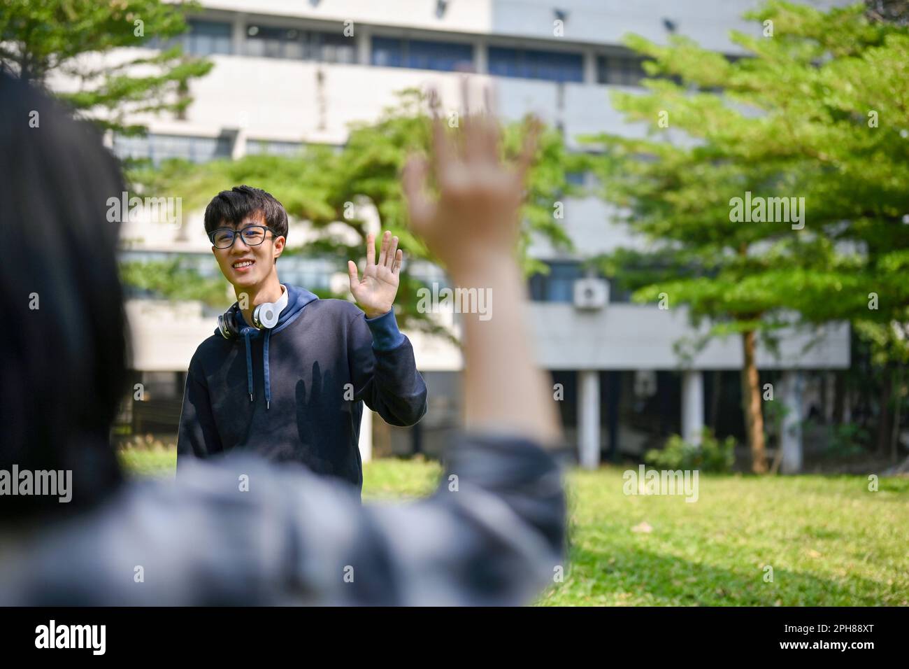 Happy and smiling young Asian male college student waves his hand to ...