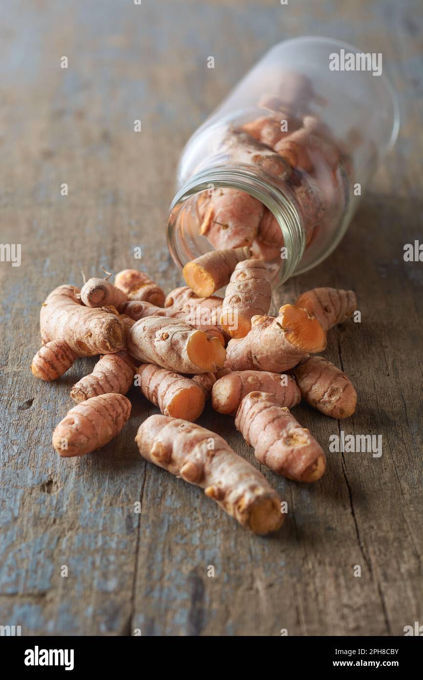 cleaned turmeric rhizomes or roots scattered on table top with a glass bottle, curcuma longa, commonly used spice in cooking and medicine Stock Photo